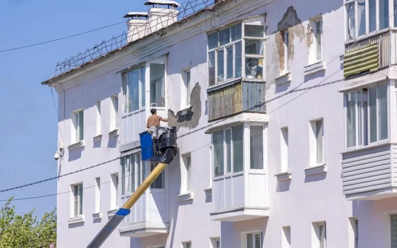 Worker renovating building facade using cherry picker on a sunny day.