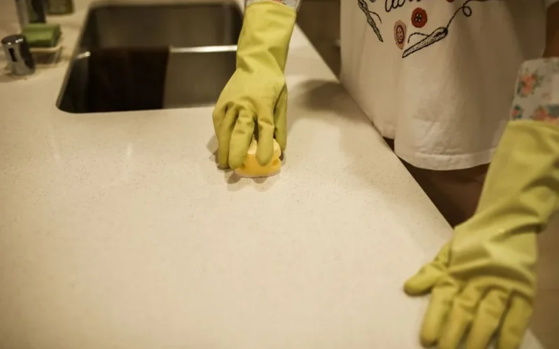 Woman using yellow rubber gloves to clean a kitchen counter with a sponge.