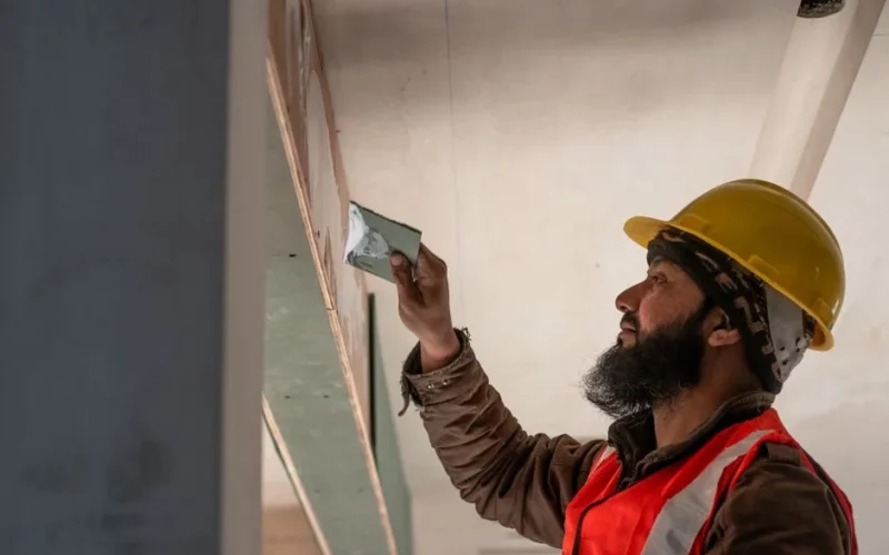 Construction worker in Delhi applies plaster to ceiling, showcasing renovation skills.