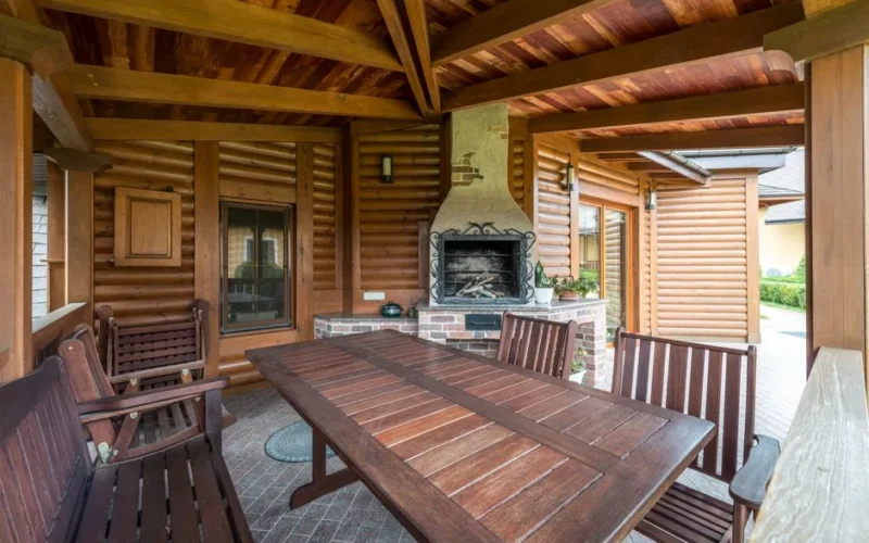 Wooden table and benches in terrace with fireplace under roof near building in daytime