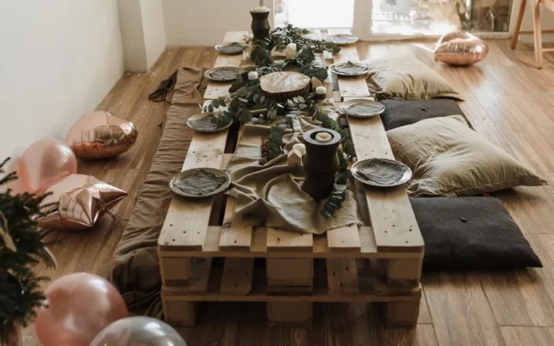 A cozy indoor party setup featuring a wooden pallet table, decorations, and casual seating.
