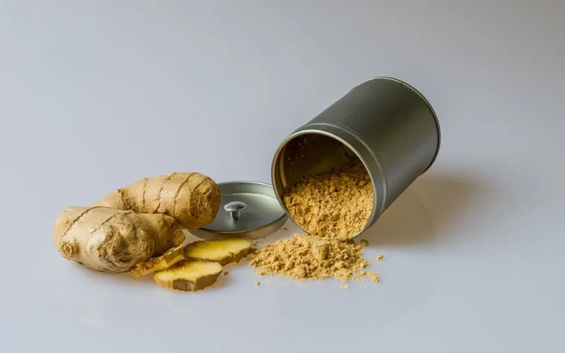Close-up of fresh ginger root with sliced pieces and ginger powder spilled from a metal container.