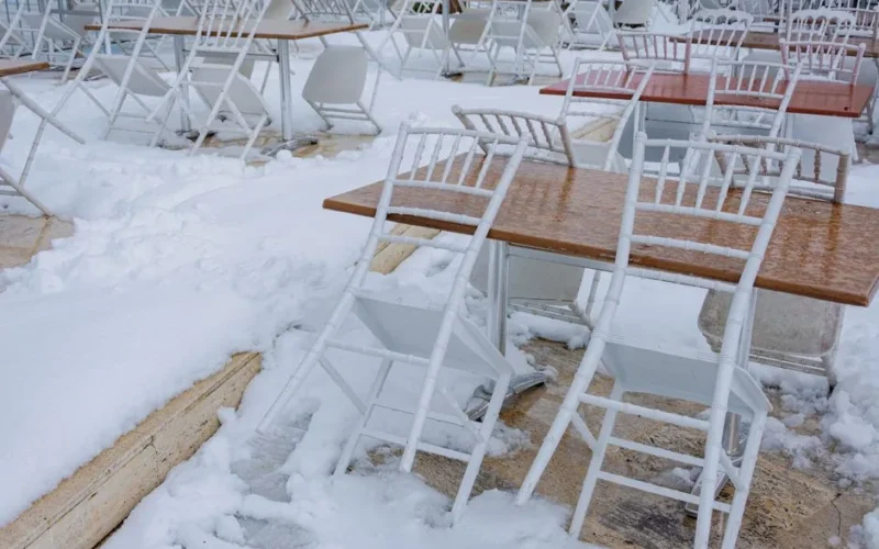 White chairs and tables covered in snow on an outdoor patio during winter.
