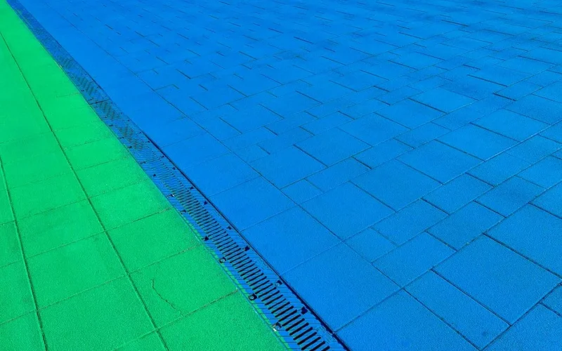 Vibrant green and blue pavement design with a drainage detail, captured outdoors.