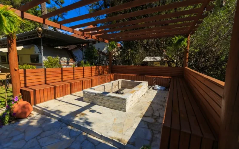 Inviting patio with a stone fire pit and wooden benches under a pergola, perfect for outdoor relaxation.