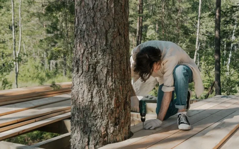 A man performs manual labor using a drill on a forest boardwalk construction project.