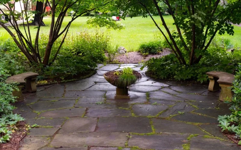 Peaceful stone patio surrounded by greenery and a central plant centerpiece in a New York garden.