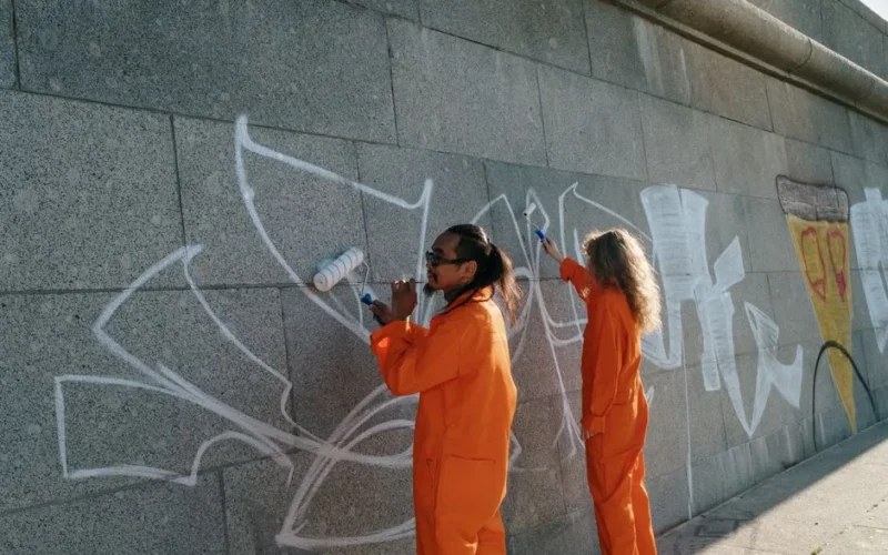 Two individuals cleaning graffiti from a concrete wall in an urban area.