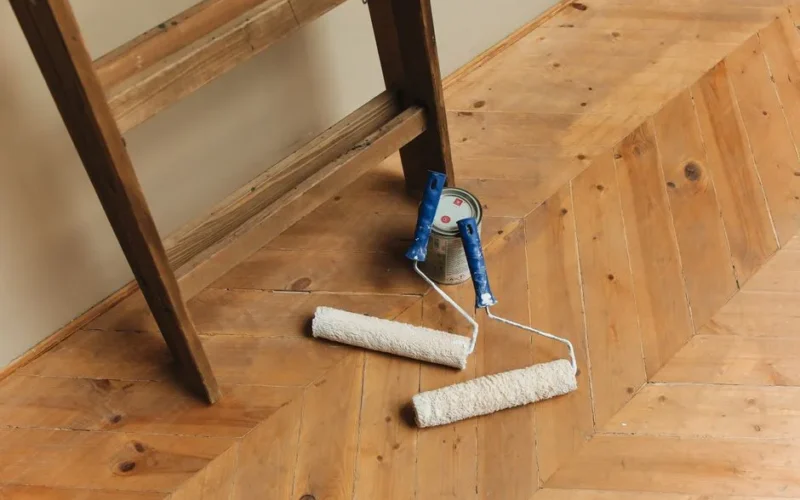 Paint rollers and ladder on a wooden floor, perfect for DIY renovation projects.