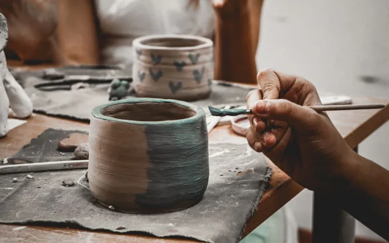 Close-up of hands skillfully painting pottery, capturing creativity and craftsmanship at work.
