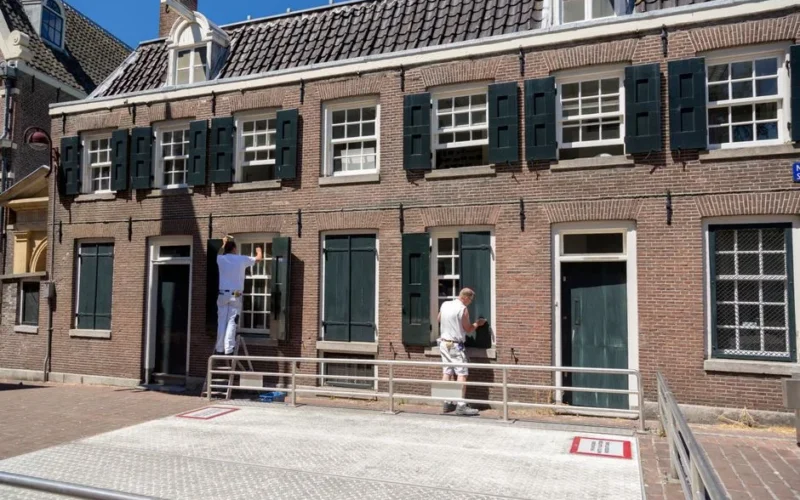 Two painters refurbishing the traditional Dutch brick house facade on a sunny day.