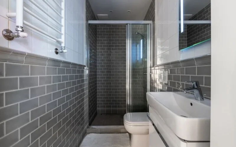 Compact bathroom featuring sleek fixtures and gray subway tiles with a glass-enclosed shower area.