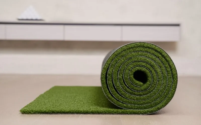 Close-up of a rolled artificial turf mat on a floor, ideal for indoor golf practice.