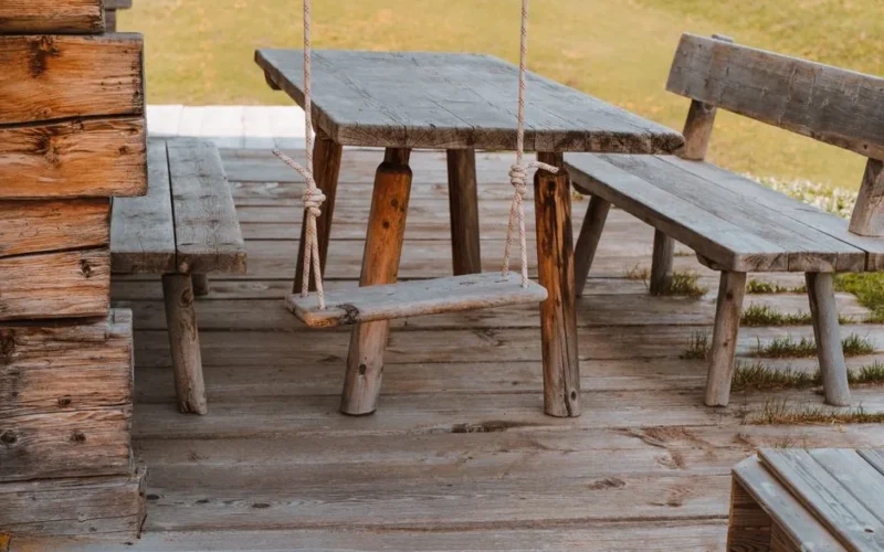 A rustic wooden bench and swing set on a sunny patio in Sankt Ulrich, Italy.