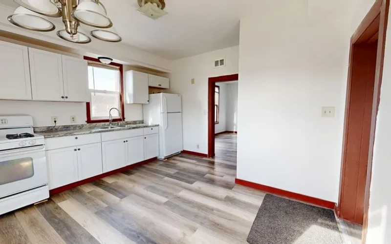 Spacious bright kitchen with white cabinets and wood flooring.