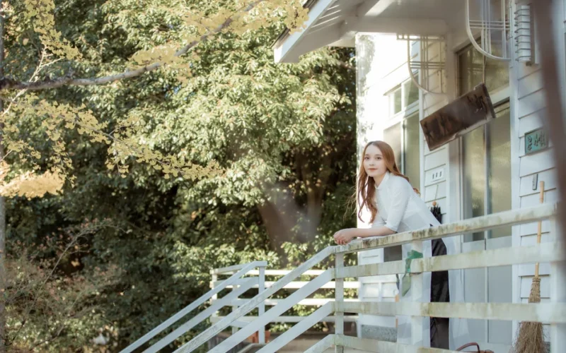 A serene outdoor scene with a woman leaning on a porch railing surrounded by lush greenery.