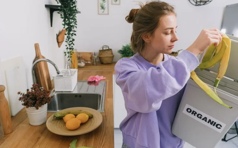 A woman composts banana peels in an indoor organic bin, promoting sustainable living.