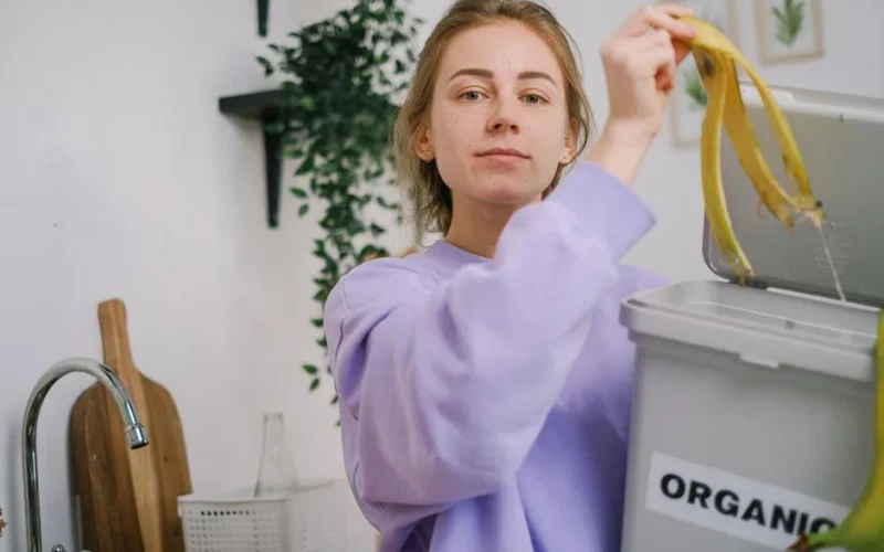 Woman disposing banana peel in organic bin at home kitchen, promoting eco-friendly lifestyle.