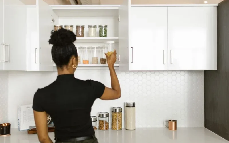 A woman organizing a pantry shelf with various food jars in a modern kitchen.