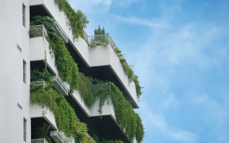 A residential building showcasing lush vertical gardens on multiple balconies against a clear blue sky.