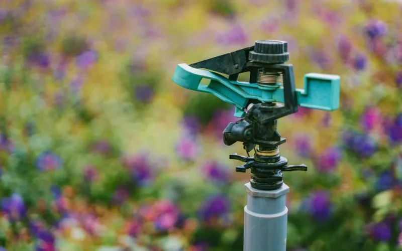 Detailed close-up of a garden sprinkler with colorful flowers in soft focus background.