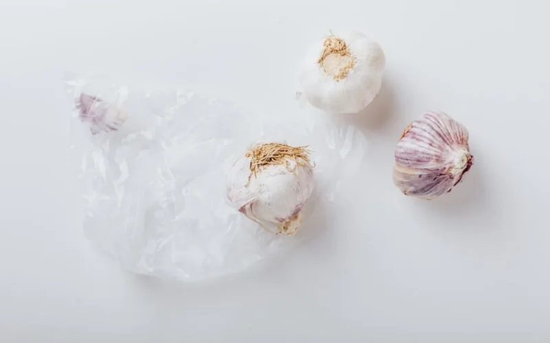 Three fresh garlic bulbs with purple streaks arranged on a white surface in an artistic flat lay style.