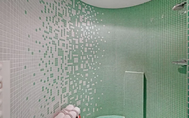 A stylish small bathroom with green and white mosaic tiles and a neatly folded towel set.
