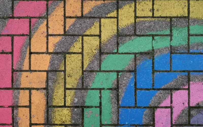 Vibrant rainbow colors painted on textured brick pavement create an urban abstract design.