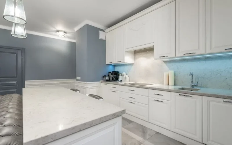 Sleek modern kitchen design featuring white cabinets, marble countertop, and ambient lighting for a minimalist look.