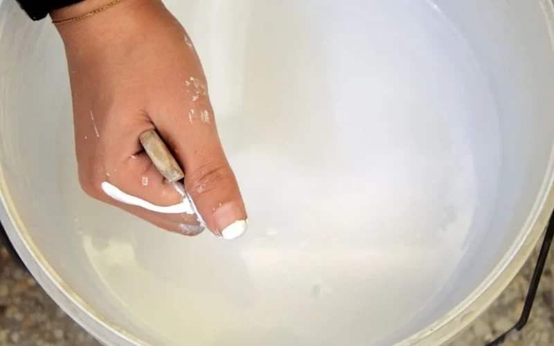 Close-up of a hand mixing white paint with a stick inside a bucket in Fès, Morocco.