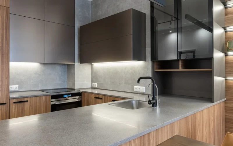Interior of contemporary gray kitchen counter with sink and faucet placed near wooden cupboards and stove in modern apartment at home