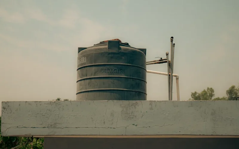 A black water storage tank placed on a rooftop with pipes, under a clear sky.