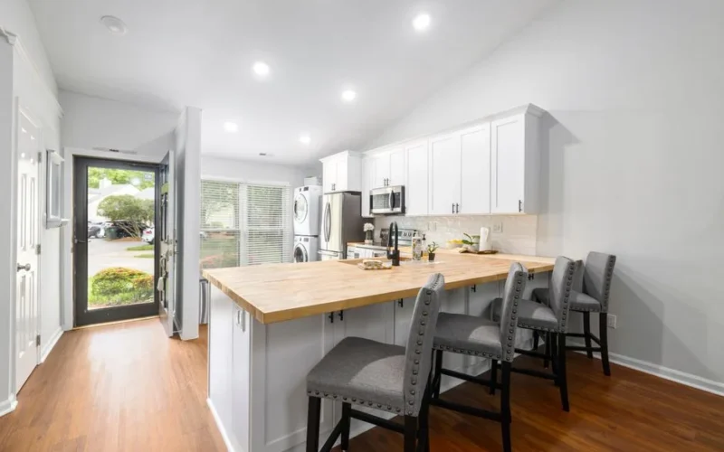 A bright modern kitchen with a wooden countertop, white cabinets, and bar stools.