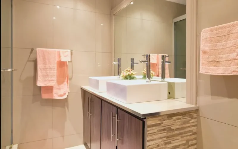 A modern bathroom featuring double sinks, large mirror, and peach towels enhancing elegance.
