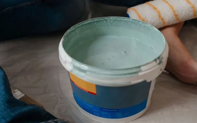 A close-up view of a bucket filled with mint green paint and a paint roller, perfect for home renovation projects.