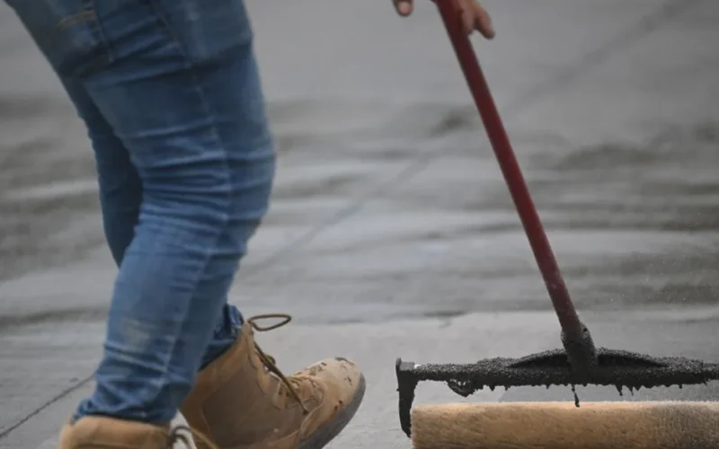 Detailed image of concrete sealing with a roller on pavement, showing boots and jeans in action.