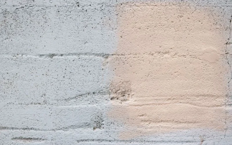 Close-up of a textured concrete wall with different paint layers in soft pink and gray.