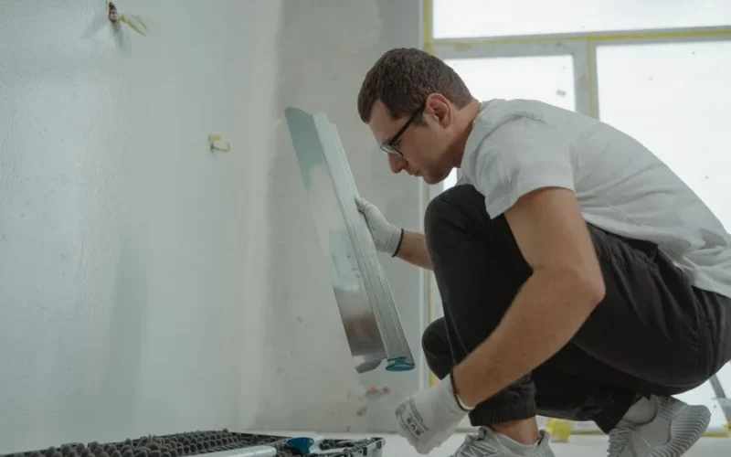 Adult male using metal trowel in interior home renovation project. White walls.