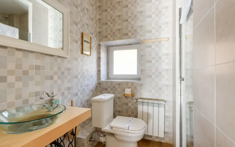 Bright bathroom featuring a contemporary glass sink, modern tiles, and natural light through the window.