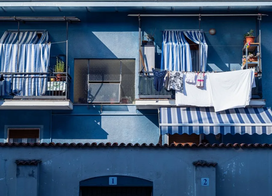 A blue balcony in Piemont, Italy with striped awnings and hanging laundry, capturing urban life.