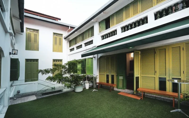 Bright courtyard with vintage green shutters and artificial grass, offering a cozy outdoor space.